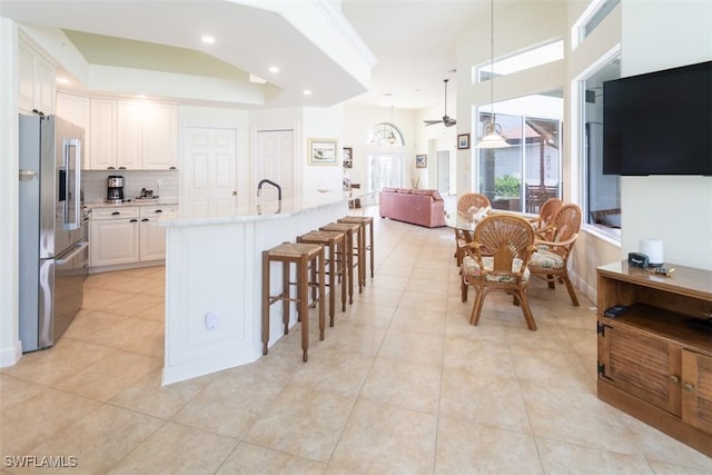 kitchen featuring decorative light fixtures, stainless steel fridge with ice dispenser, an island with sink, white cabinetry, and light tile patterned flooring