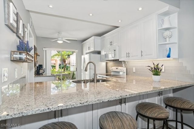 kitchen with white cabinetry, sink, white appliances, and kitchen peninsula