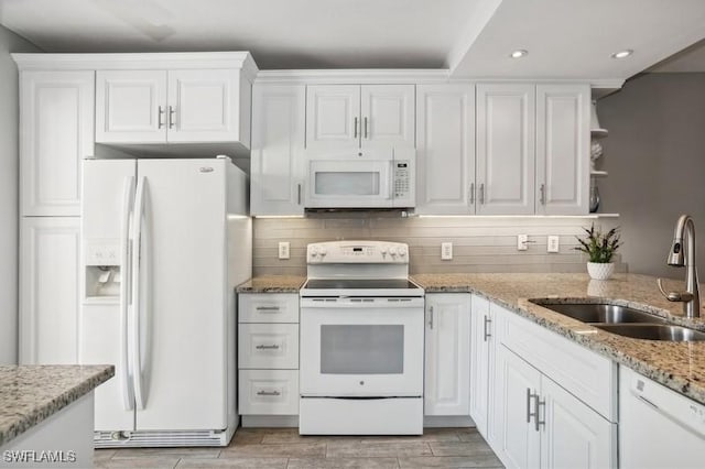 kitchen with sink, white appliances, white cabinetry, backsplash, and light stone countertops