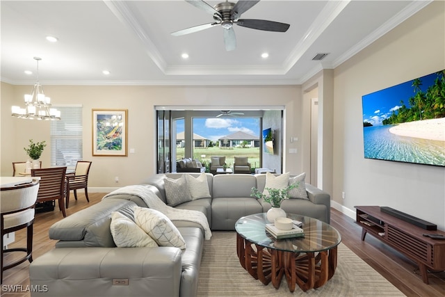 living room featuring crown molding, wood-type flooring, ceiling fan with notable chandelier, and a raised ceiling