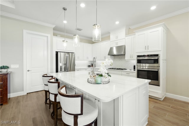 kitchen featuring appliances with stainless steel finishes, hanging light fixtures, white cabinetry, and an island with sink