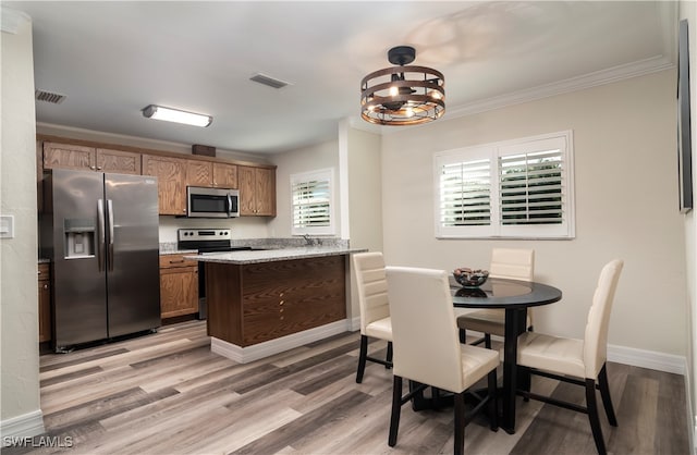 kitchen featuring appliances with stainless steel finishes, crown molding, light hardwood / wood-style floors, a notable chandelier, and light stone counters