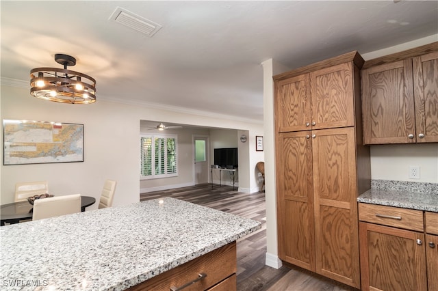 kitchen featuring dark wood-type flooring, hanging light fixtures, crown molding, light stone counters, and ceiling fan with notable chandelier