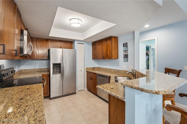 kitchen featuring a kitchen bar, a peninsula, stainless steel appliances, a raised ceiling, and a sink