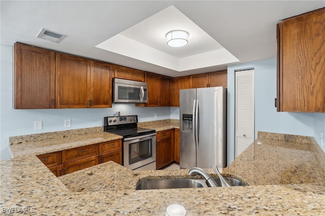 kitchen with sink, appliances with stainless steel finishes, light stone counters, and a raised ceiling