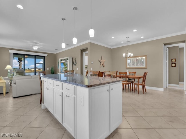 kitchen with a kitchen island, hanging light fixtures, dark stone counters, white cabinets, and crown molding