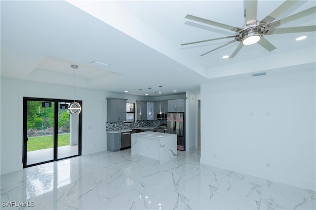 kitchen with gray cabinetry, stainless steel appliances, a raised ceiling, and a kitchen island