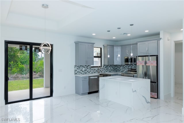 kitchen with a kitchen island, appliances with stainless steel finishes, backsplash, light stone countertops, and pendant lighting