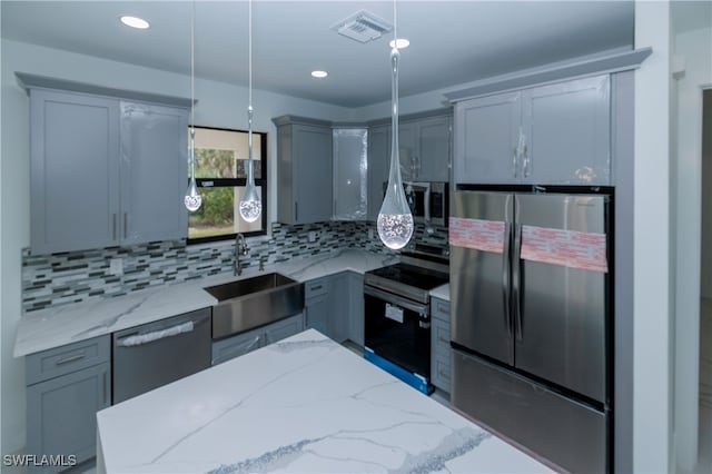 kitchen featuring light stone countertops, sink, backsplash, stainless steel appliances, and decorative light fixtures