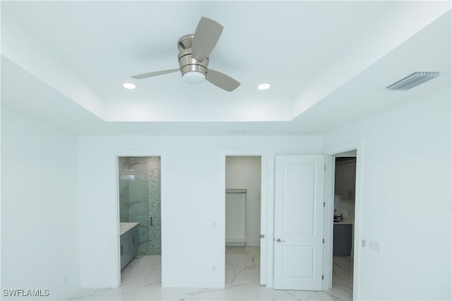 unfurnished bedroom with a spacious closet, a raised ceiling, a closet, ceiling fan, and connected bathroom