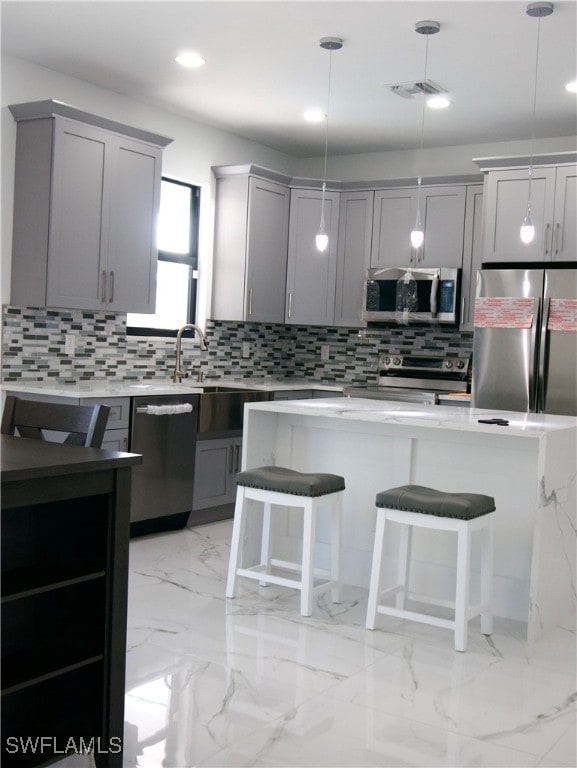 kitchen featuring gray cabinets, a breakfast bar, stainless steel appliances, and pendant lighting