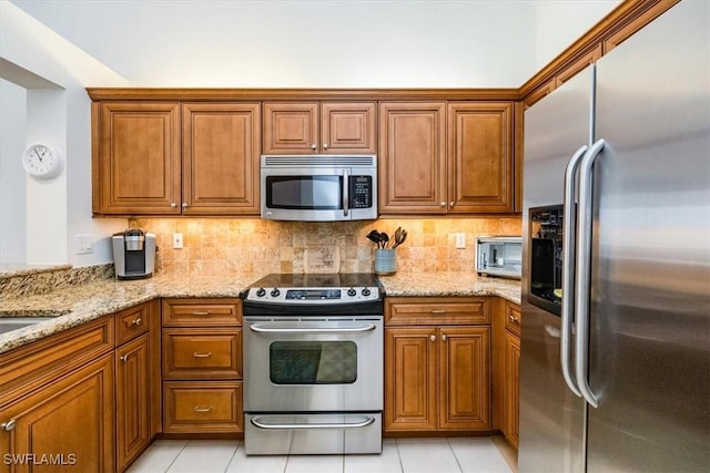 7725 Pebble Creek Cir Unit 8-303, Naples, FL 34108 - kitchen featuring appliances with stainless steel finishes, brown cabinets, light stone counters, and light tile patterned floors