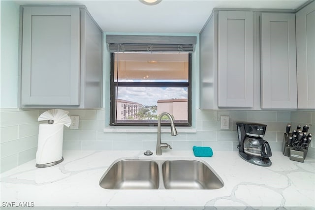 kitchen with backsplash, light stone countertops, and a sink