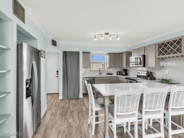 kitchen with a sink, gray cabinets, stainless steel appliances, a peninsula, and ornamental molding