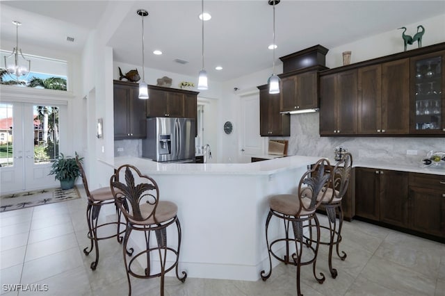 kitchen with a kitchen breakfast bar, stainless steel fridge, pendant lighting, decorative backsplash, and a chandelier