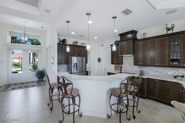 kitchen featuring decorative backsplash, stainless steel fridge, dark brown cabinets, a kitchen bar, and decorative light fixtures