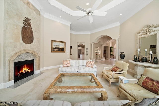 living room featuring a fireplace, ceiling fan, ornamental molding, decorative columns, and light colored carpet