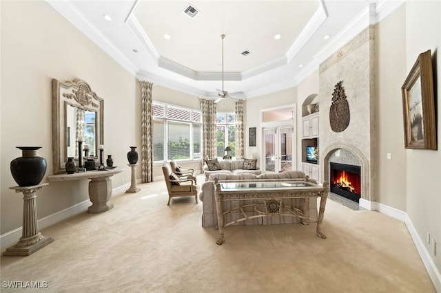 living room with light carpet, a large fireplace, ornamental molding, ceiling fan, and a tray ceiling