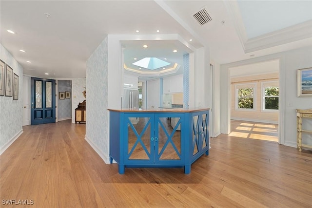 interior space featuring stainless steel refrigerator, a skylight, crown molding, a tray ceiling, and light wood-type flooring