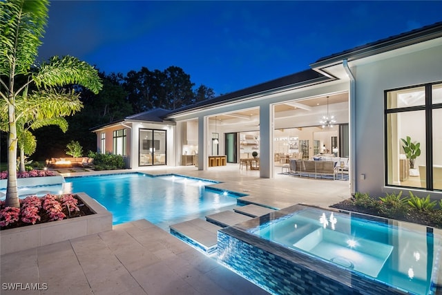 pool at twilight featuring an in ground hot tub, pool water feature, and a patio