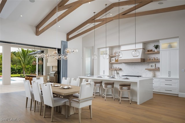 dining space with beam ceiling, sink, high vaulted ceiling, and light hardwood / wood-style flooring