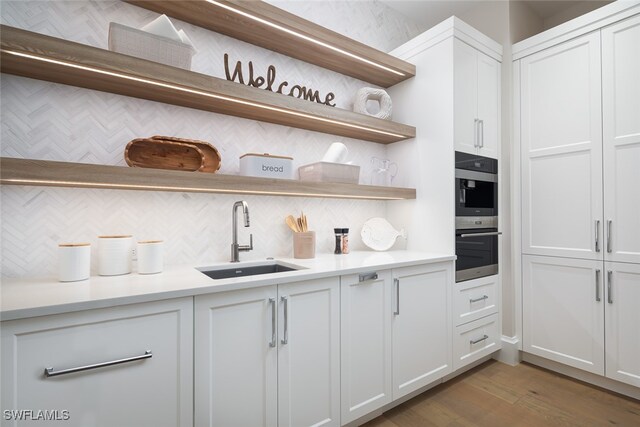 kitchen featuring white cabinets, light wood-type flooring, stainless steel double oven, and sink