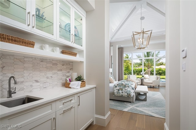 bar with pendant lighting, backsplash, sink, light hardwood / wood-style flooring, and white cabinetry