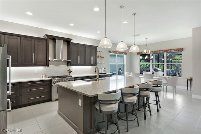 kitchen featuring a kitchen island with sink, wall chimney range hood, hanging light fixtures, stainless steel appliances, and sink