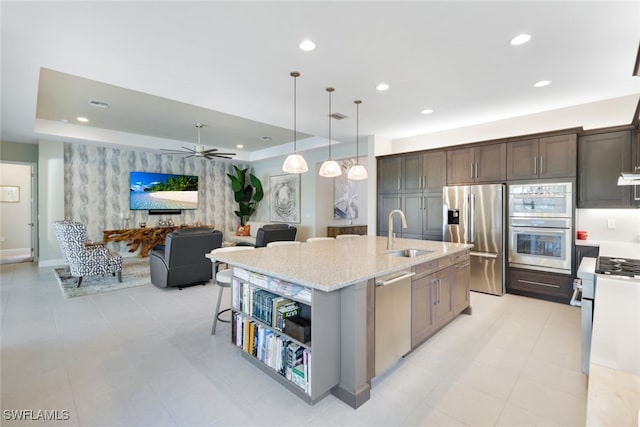 kitchen with a kitchen island with sink, stainless steel appliances, dark brown cabinets, sink, and light stone counters