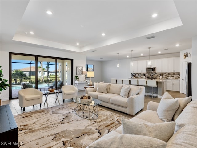 living room with light wood-type flooring and a raised ceiling