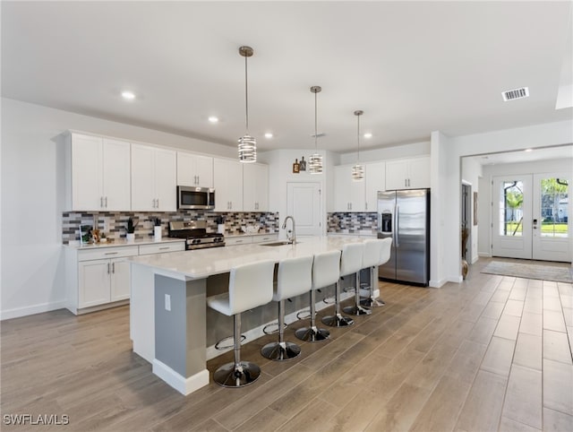 kitchen with light wood-type flooring, stainless steel appliances, a kitchen island with sink, sink, and white cabinets