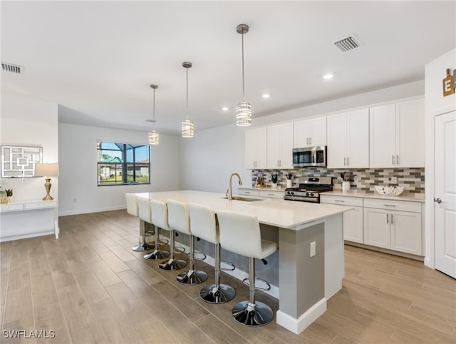 kitchen with pendant lighting, sink, light wood-type flooring, appliances with stainless steel finishes, and white cabinetry