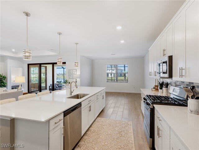 kitchen with a center island with sink, sink, light wood-type flooring, appliances with stainless steel finishes, and decorative light fixtures