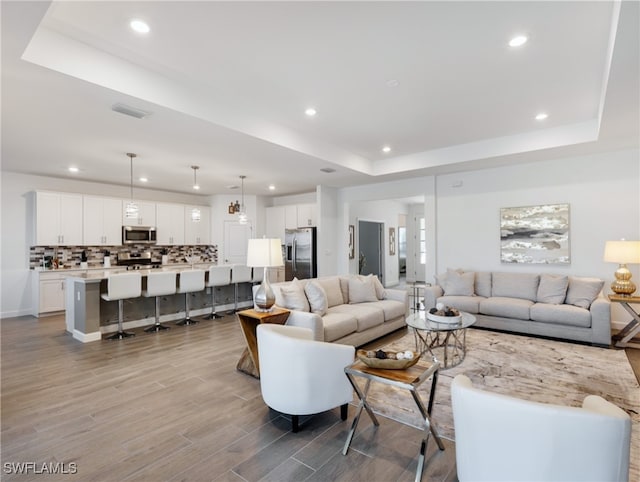 living room with a raised ceiling and light wood-type flooring