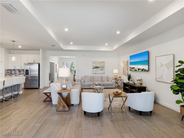 living room with a raised ceiling and light wood-type flooring