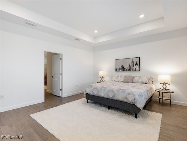 bedroom with a raised ceiling and wood-type flooring