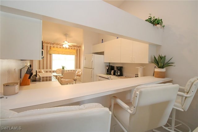 kitchen featuring kitchen peninsula, ceiling fan, white fridge, white cabinetry, and a breakfast bar area