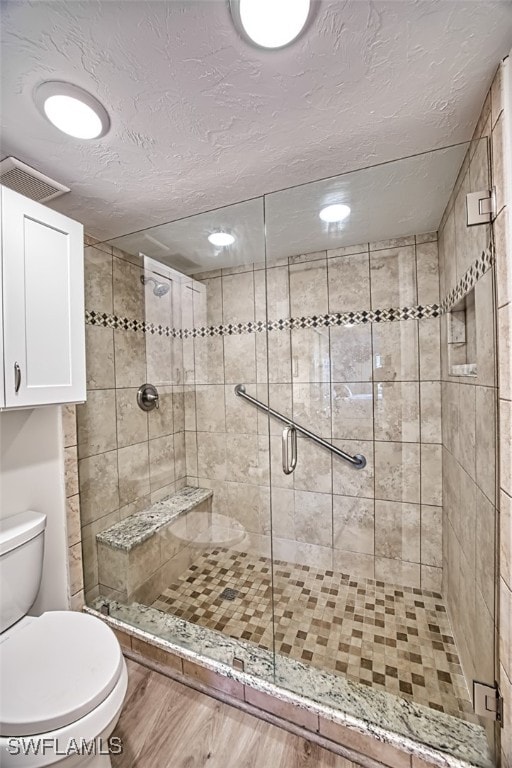 bathroom with toilet, hardwood / wood-style floors, a textured ceiling, and a shower with door