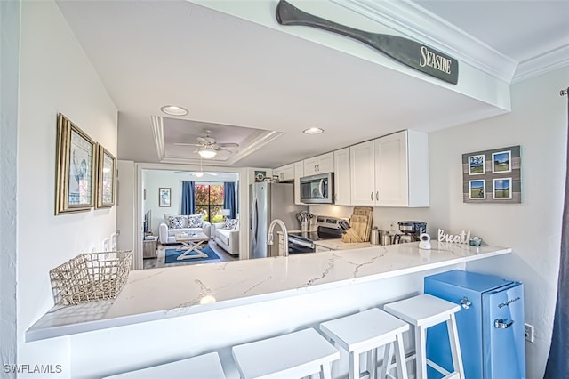 kitchen with kitchen peninsula, stainless steel appliances, crown molding, a kitchen bar, and white cabinetry