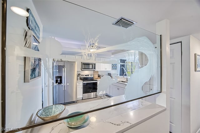 kitchen with white cabinets, stainless steel appliances, sink, and light stone counters