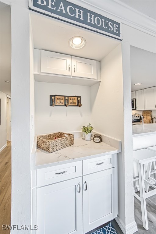 bar with white cabinetry, hardwood / wood-style floors, and light stone countertops