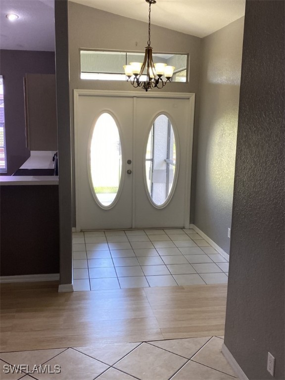 foyer featuring french doors, light wood-type flooring, vaulted ceiling, and a chandelier