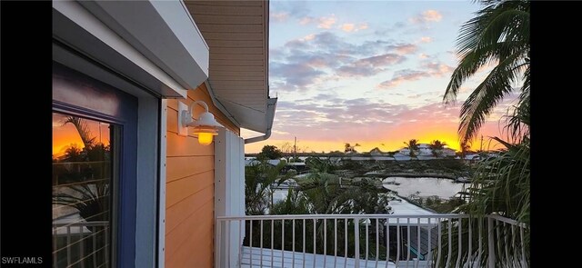 balcony at dusk featuring a water view