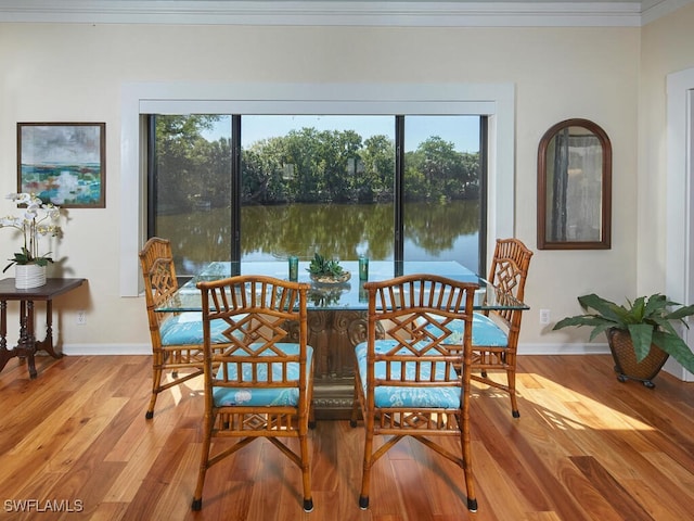 dining area with ornamental molding, light hardwood / wood-style flooring, a water view, and a healthy amount of sunlight