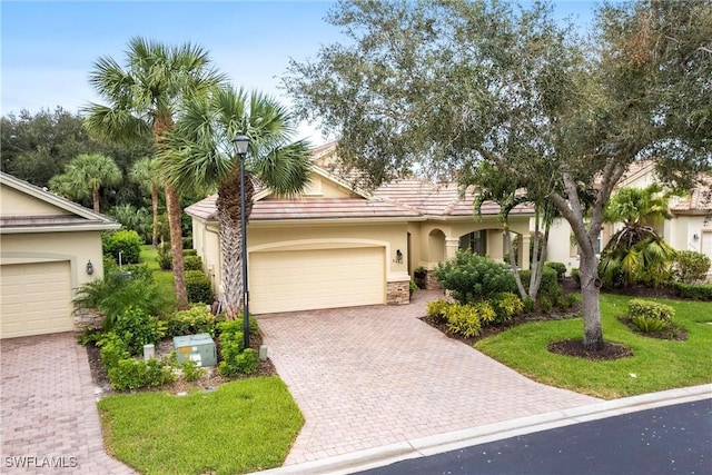 view of front of house with a garage, a front lawn, stone siding, decorative driveway, and stucco siding