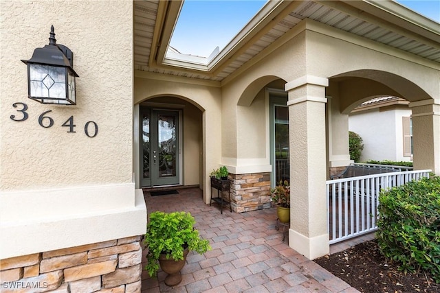 property entrance with stucco siding, a porch, and stone siding