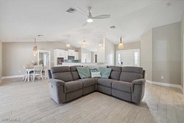 living room with light hardwood / wood-style flooring, ceiling fan with notable chandelier, and vaulted ceiling