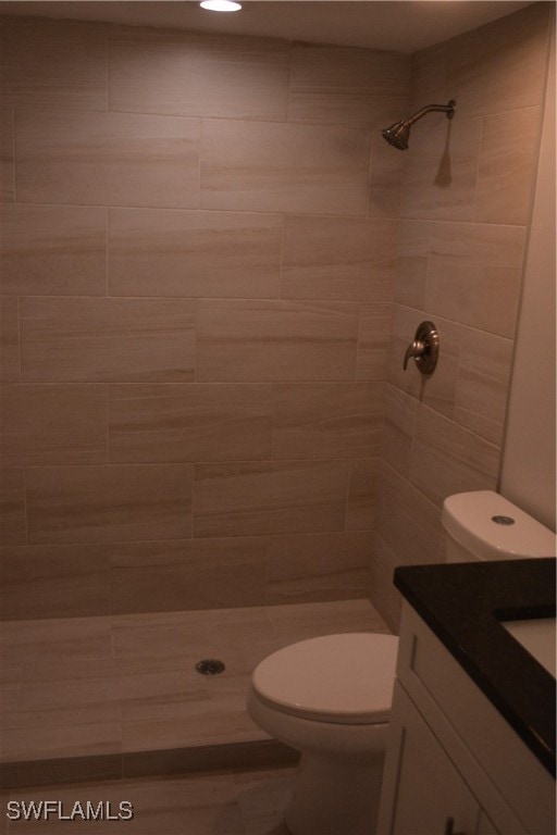 bathroom with a tile shower, toilet, and vanity