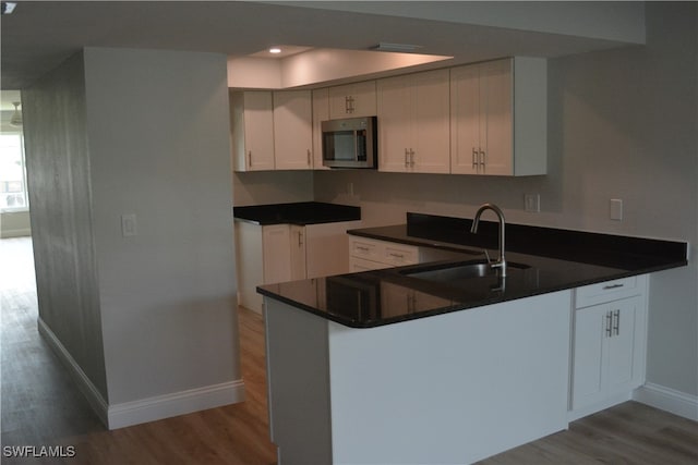 kitchen featuring white cabinets, dark stone countertops, sink, kitchen peninsula, and light wood-type flooring