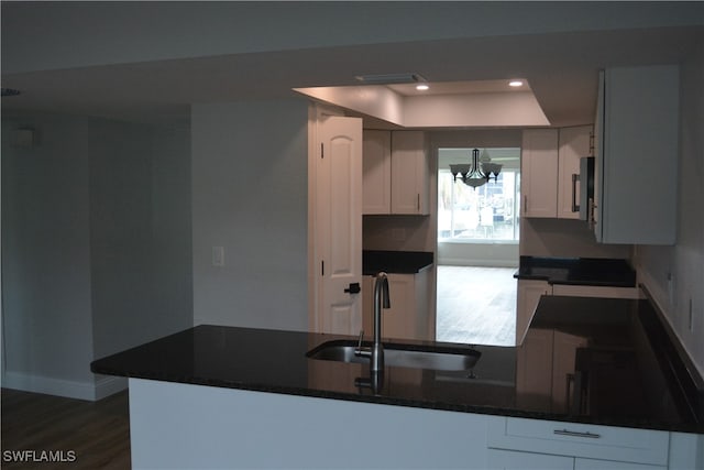 kitchen with white cabinets, sink, kitchen peninsula, a notable chandelier, and a tray ceiling